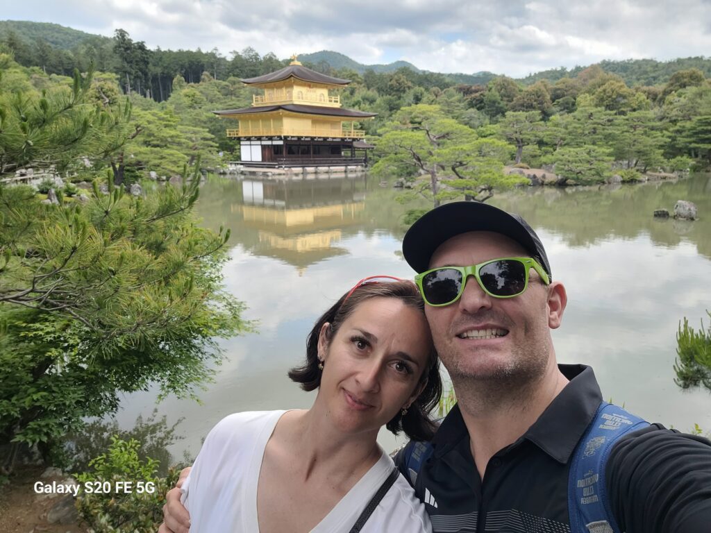 Andrew Smith and Bibian couple taking a selfie in front of the Kinkaku ji Golden Pavilion in Kyoto Japan with phone watermark.